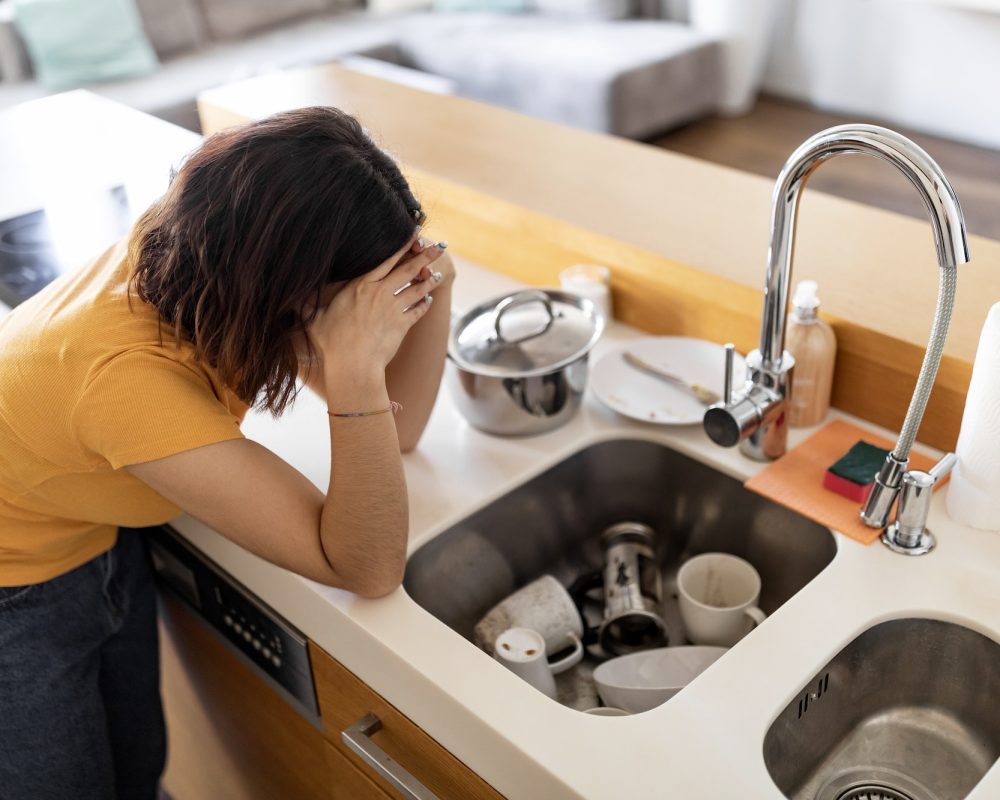 Domestic Chores Stress. Depressed Housewife Looking At Dirty Dishes In Sink