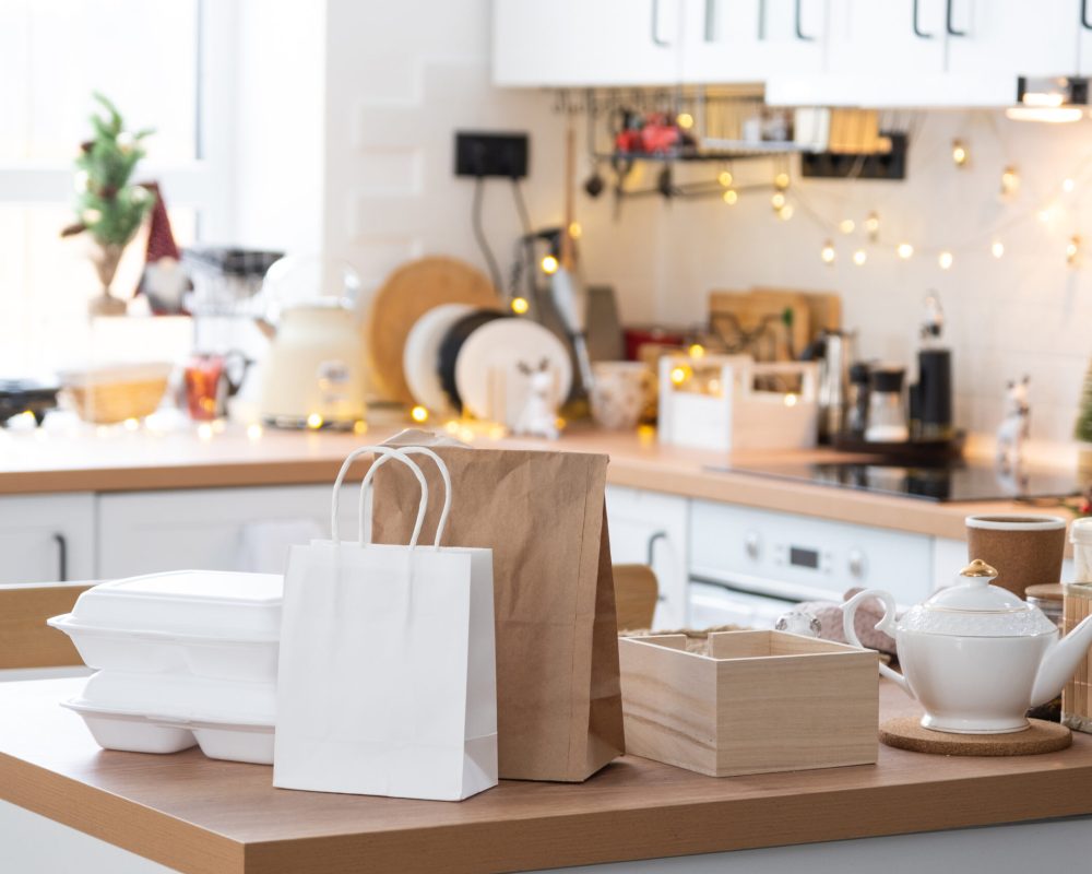 Food delivery service containers on table white scandi festive kitchen in christmas decor. Eve New year, saving time, too lazy to cook, hot order, disposable plastic box in fairy light. mock up